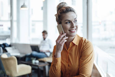 Smiling entrepreneur talking on mobile phone with colleague in background at cafe - JOSEF04514