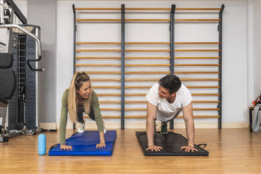 Smiling male and female athletes doing push-ups on exercise mat in gym - RSGF00679