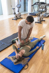 Sportsman helping female friend in exercising at gym - RSGF00681