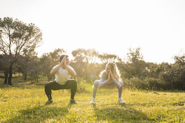 Young friends crouching while exercising together at grass area - RSGF00686