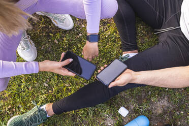 Male and female friends holding mobile phone while sitting on grass - RSGF00689