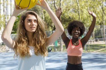 Junge Frau hält Basketball mit Freund im Hintergrund im Park - IFRF00581
