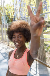 Lächelnde Frau mit lockigem Haar, die im Park ein Friedenszeichen macht - IFRF00585