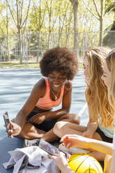 Cheerful young woman showing mobile phone to female friends in park - IFRF00591