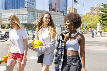 Weibliche Freunde unterhalten sich bei einem Spaziergang auf der Straße an einem sonnigen Tag - IFRF00621