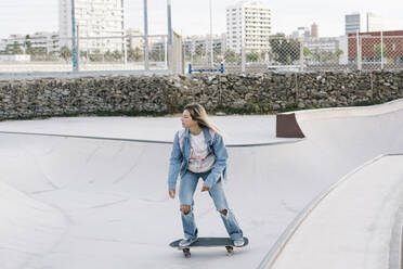 Mittlere erwachsene Frau schaut weg, während sie im Park Skateboard fährt - XLGF01783