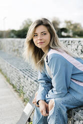 Blond woman looking away while sitting on bench at skateboard park - XLGF01794