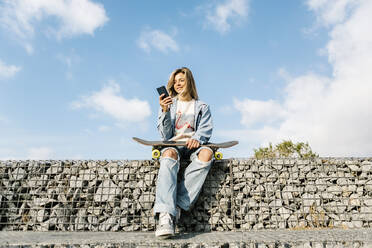 Lächelnde Frau mit Mobiltelefon an einer Felswand sitzend - XLGF01795