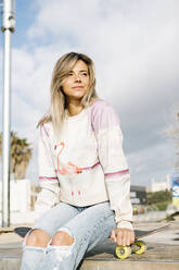 Smiling woman sitting on skateboard at park - XLGF01797