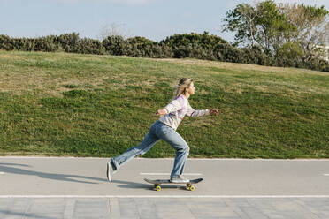 Mid adult woman skateboarding on road - XLGF01799