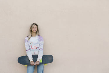 Blonde Frau mit Skateboard an der Wand lehnend - XLGF01801