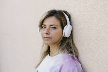 Frau mit Kopfhörern hört Musik, während sie sich an die Wand lehnt - XLGF01802