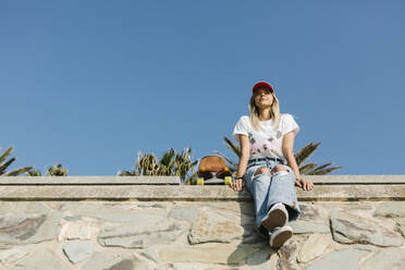 Mid adult woman wearing cap sitting on retaining wall - XLGF01810