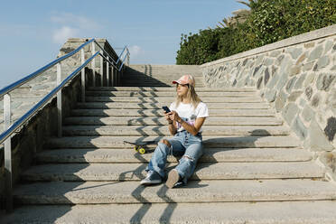 Mittlere erwachsene Frau mit Mobiltelefon, die auf einer Treppe sitzend an einem sonnigen Tag nachdenkt - XLGF01813