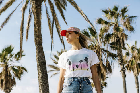 Woman standing below palm tree during sunny day - XLGF01818