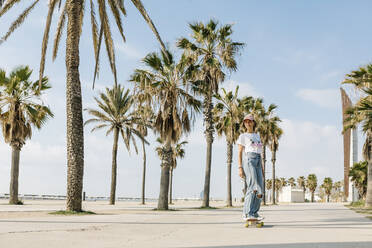Mid adult woman skating by palm tree on footpath - XLGF01819