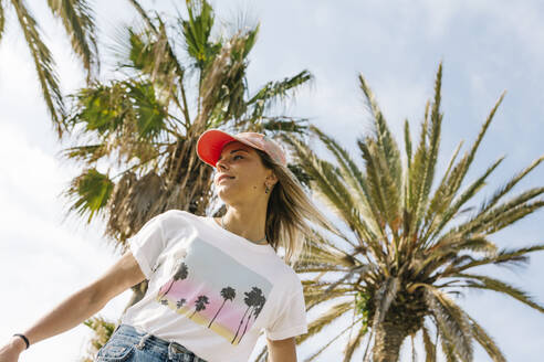 Mid adult woman wearing cap below tree - XLGF01820