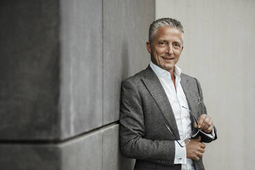 Smiling businessman standing in front of gray wall - SAJF00129