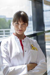 Confident female professional with arms crossed standing by glass wall - BMOF00644