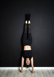 Active sportswoman doing handstand on floor in yoga studio - GIOF12615