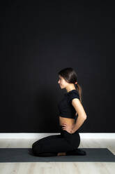 Junge Sportlerin sitzt mit der Hand auf der Hüfte im Yogastudio - GIOF12619