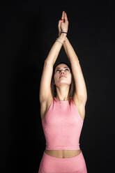 Sportswoman stretching hand while exercising in front of black background - GIOF12639