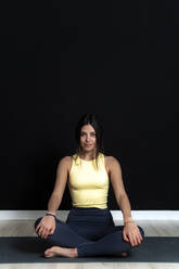Schöne Sportlerin, die im Schneidersitz auf einer Yogamatte im Yogastudio sitzt - GIOF12647