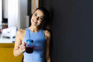 Smiling sportsperson with juice leaning on wall at home - GIOF12667