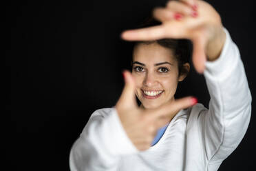 Sportswoman making finger frame in front of black background - GIOF12675