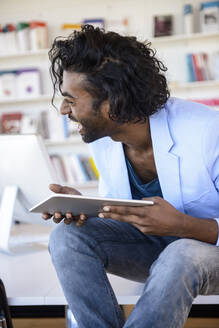 Lachender junger Mann mit digitalem Tablet in einer Bibliothek - BMOF00652