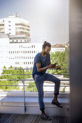 Man using smart phone while standing near railing in balcony - BMOF00660