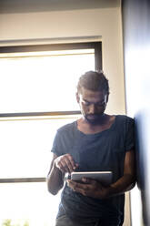 Junger Mann, der ein digitales Tablet benutzt und sich an die Wand lehnt - BMOF00666
