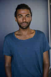 Young man wearing blue t-shirt while standing near blue wall - BMOF00668