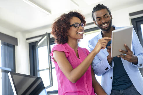 Lächelnder Mann und lächelnde Frau benutzen ein digitales Tablet im Büro - BMOF00672