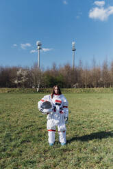 Female astronaut holding space helmet on grass area - MEUF02777