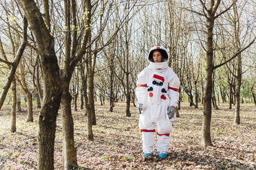Junge Astronautin im Weltraum, die an einem kahlen Baum im Wald steht und nachdenkt - MEUF02784
