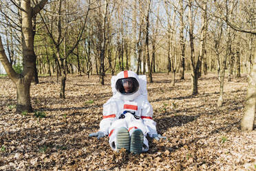 Weibliche Forscherin mit Raumanzug und Helm sitzt im Wald - MEUF02785