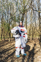 Female astronaut holding space helmet while standing in forest - MEUF02791