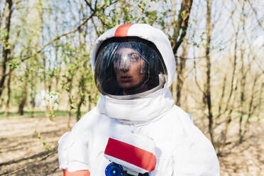 Thoughtful female explorer in space suit and helmet at forest - MEUF02793