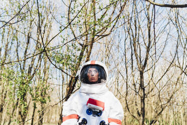 Female astronaut wearing space suit and helmet standing in forest - MEUF02795