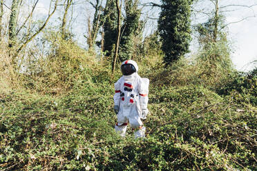 Young astronaut wearing space suit and helmet standing in bush at forest - MEUF02802