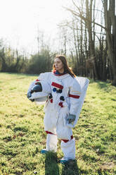 Female astronaut holding space helmet while standing on grass - MEUF02813
