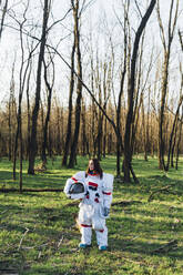 Astronautin mit Weltraumhelm im Wald stehend - MEUF02821