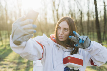 Eine Forscherin im Raumanzug macht ein Selfie mit ihrem Mobiltelefon an einem sonnigen Tag - MEUF02830