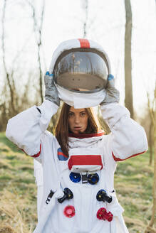 Female astronaut removing space helmet in forest - MEUF02838