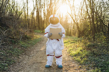 Junge Astronautin im Raumanzug hält Karton auf Waldweg - MEUF02848