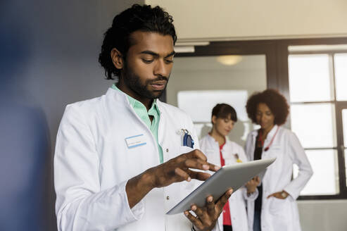 Junge männliche Mitarbeiter im Gesundheitswesen, die ein digitales Tablet benutzen, mit weiblichen Kollegen im Hintergrund im Krankenhaus - BMOF00701