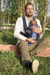 Mann sitzt mit Baby im Park an einem sonnigen Tag - VEGF04451