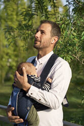 Aufmerksamer Vater kümmert sich im Park um seinen Sohn in der Babytrage - VEGF04453