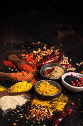 Assorted aromatic colorful spices in bowls and wooden spoons arranged on dark table with scattered condiments - ADSF24182